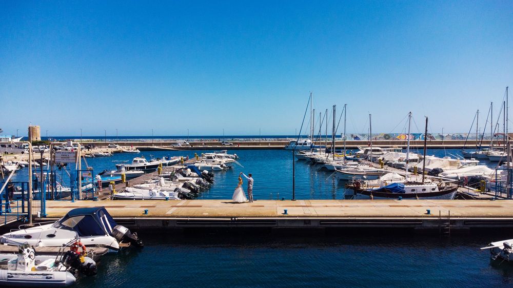 A sunny marina filled with boats and yachts docked along concrete piers with blue water and clear skies.