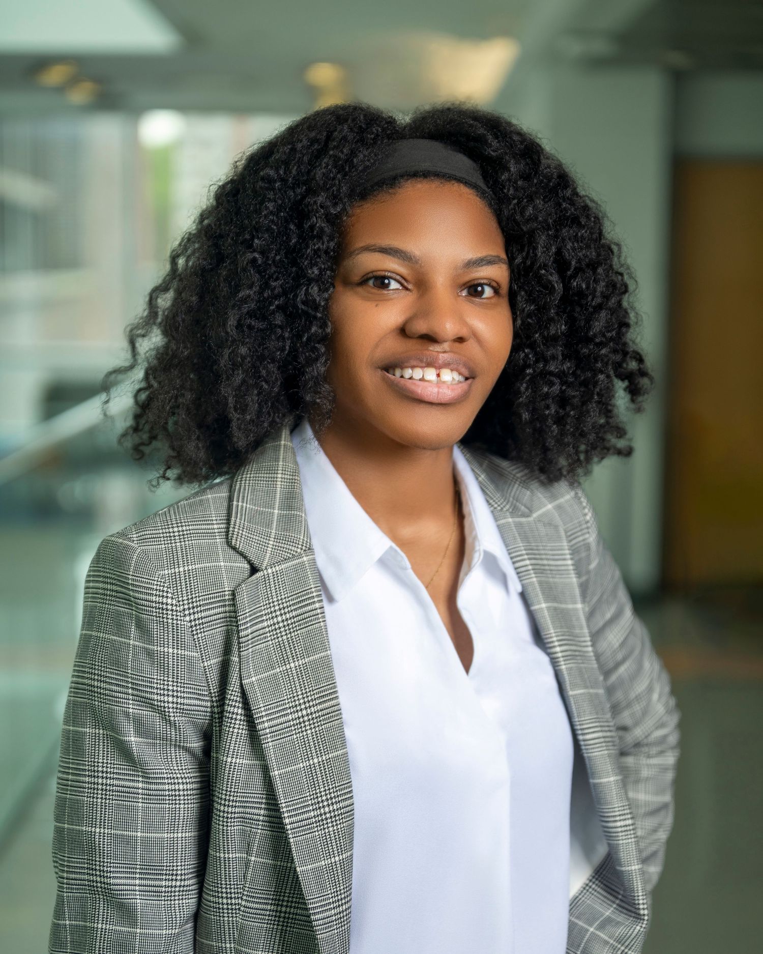 Professional portrait of someone wearing a gray plaid blazer and white shirt in an office environment.