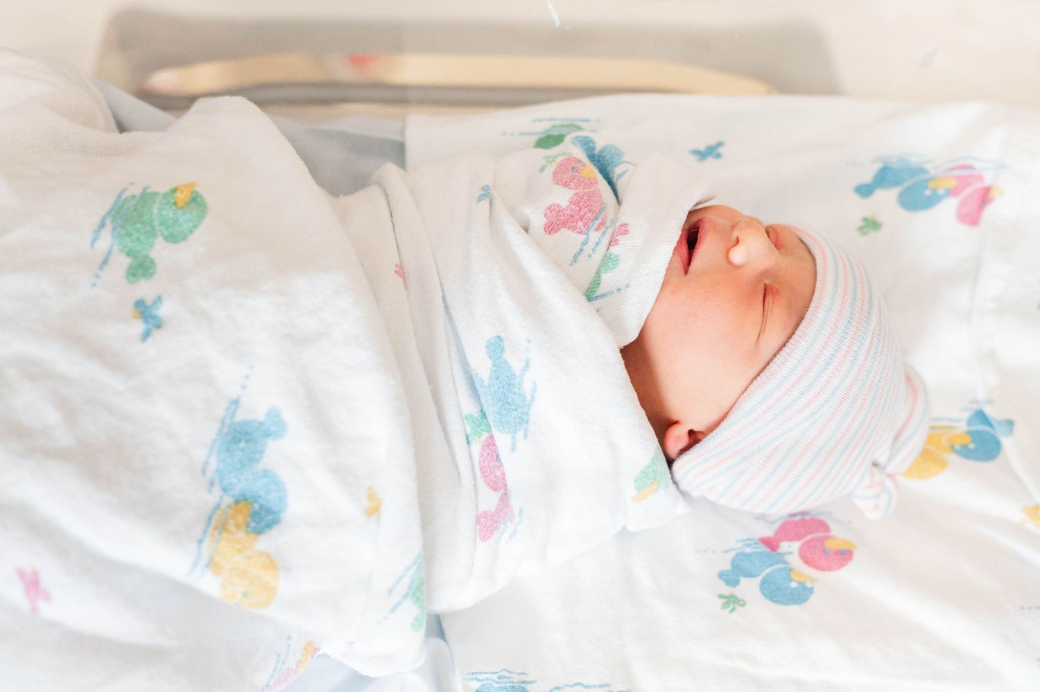 A swaddled baby rests on white bedding with colorful dinosaur print fabric.