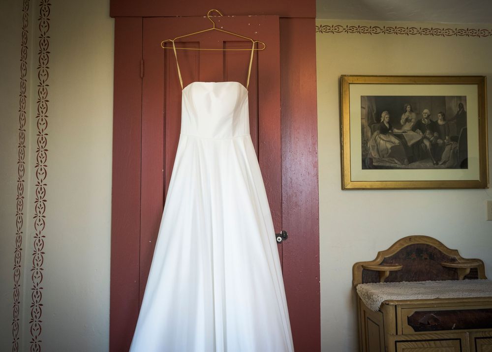 Sunlit sheer white curtains frame red wooden windows in a rustic home interior with vintage artwork on the walls.