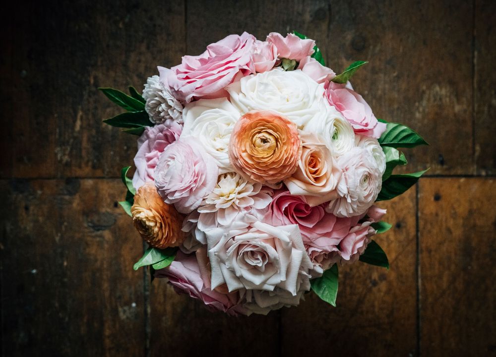 A beautiful bridal bouquet with pink, peach, and white roses arranged in a round shape on dark wooden background.
