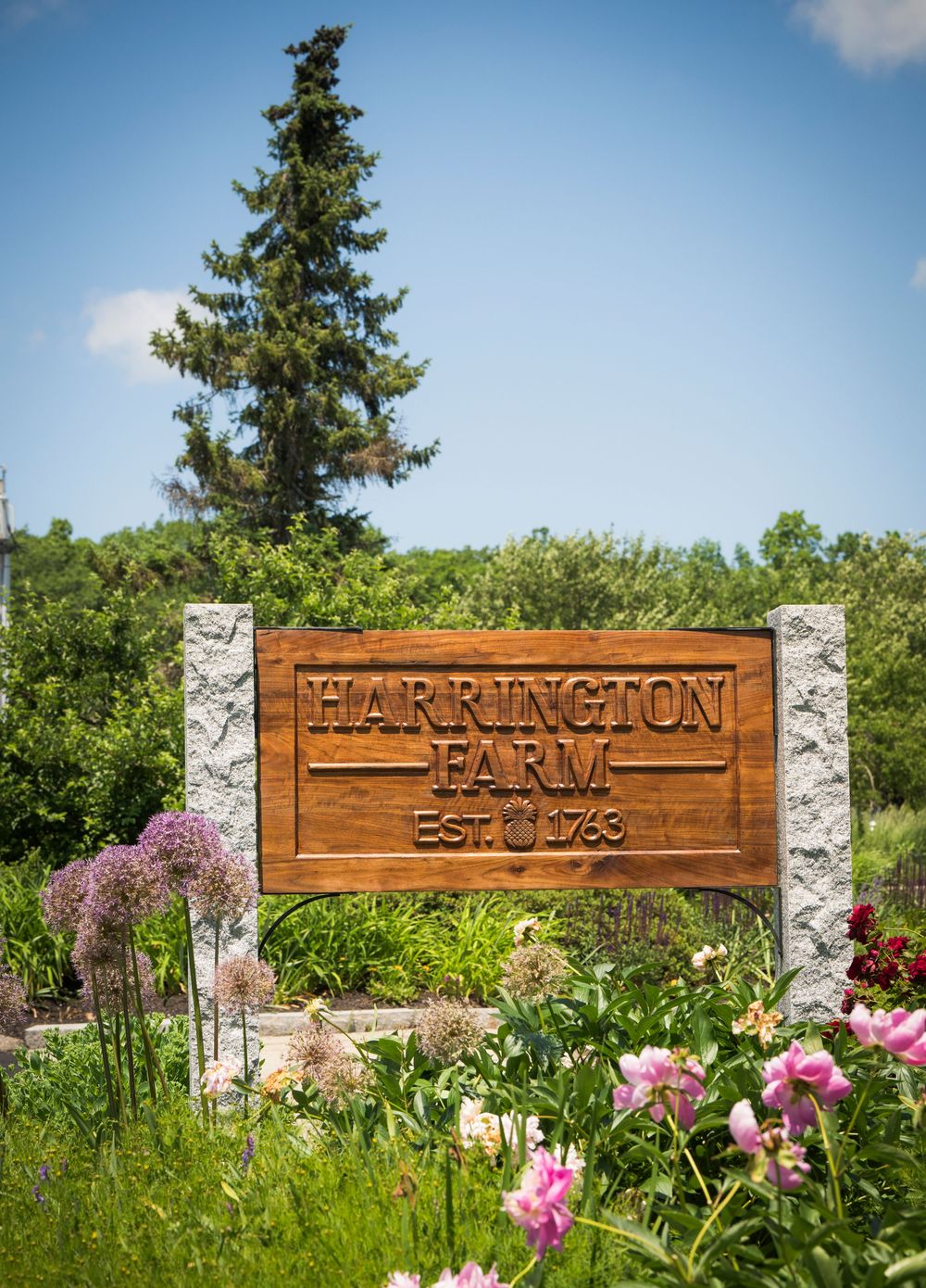 Wooden Parkington Inn Est. 1723 sign mounted on stone pillars surrounded by blooming pink flowers and greenery.