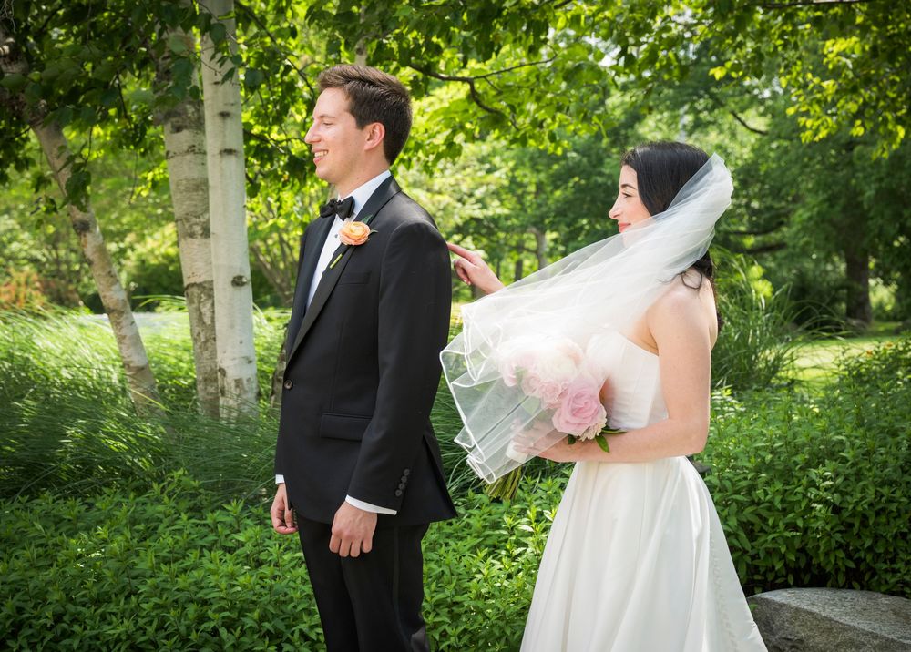 Outdoor wedding portrait showing couple walking hand in hand through a lush green garden setting.