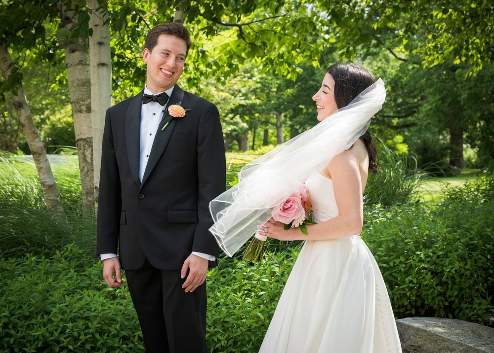 A wedding couple in formal attire sharing a candid moment outdoors in a lush green garden setting.