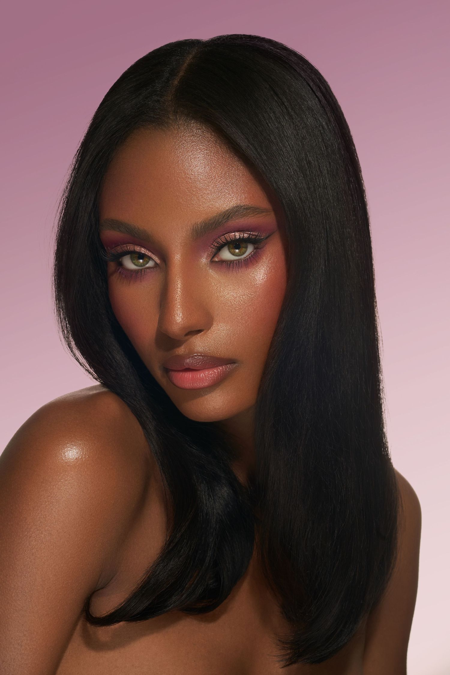 Glamour beauty portrait with pink-toned makeup and sleek dark hair against rose background.