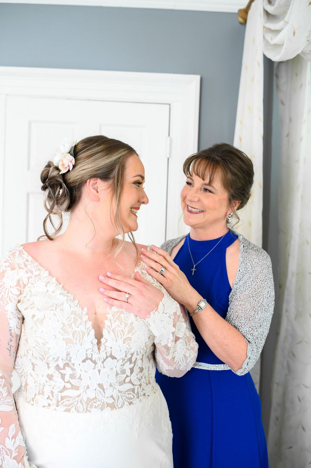 Two people share a joyful moment while getting ready, one wearing a white lace dress and another in royal blue. Primrose Cottage Wedding