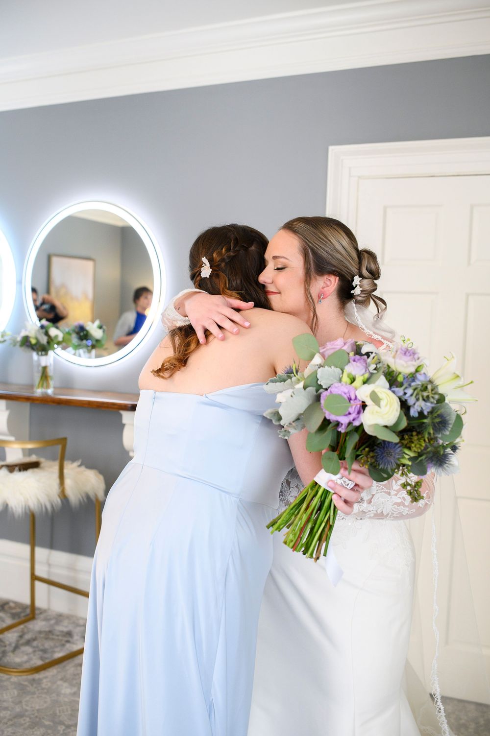 Two people embrace emotionally while holding a blue and white floral bouquet in a sunlit room. Primrose Cottage Wedding Photographs