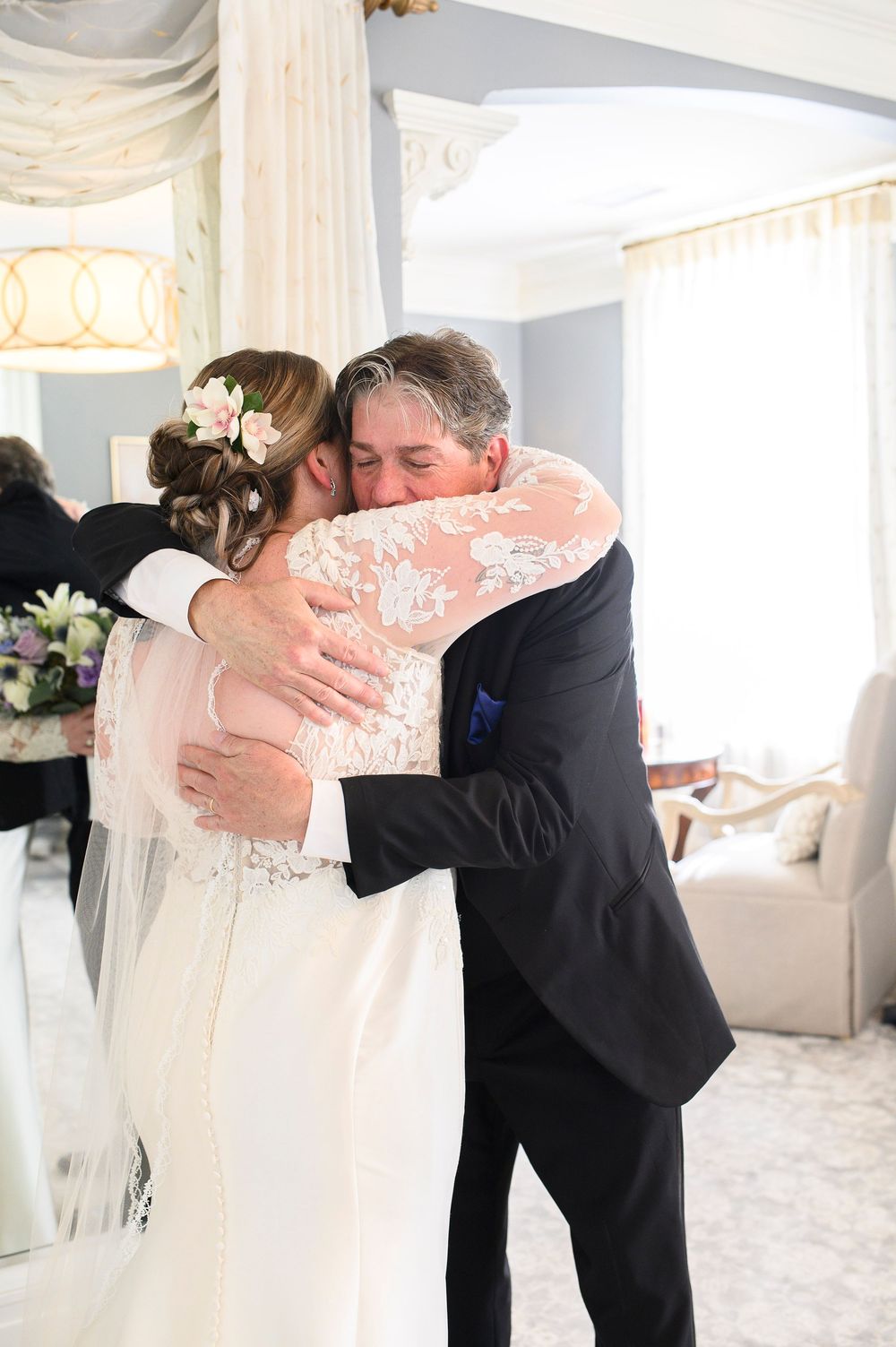 Emotional wedding moment captured with a tight embrace in a bright sunlit room with white decor and floral details. Primrose Cottage Wedding