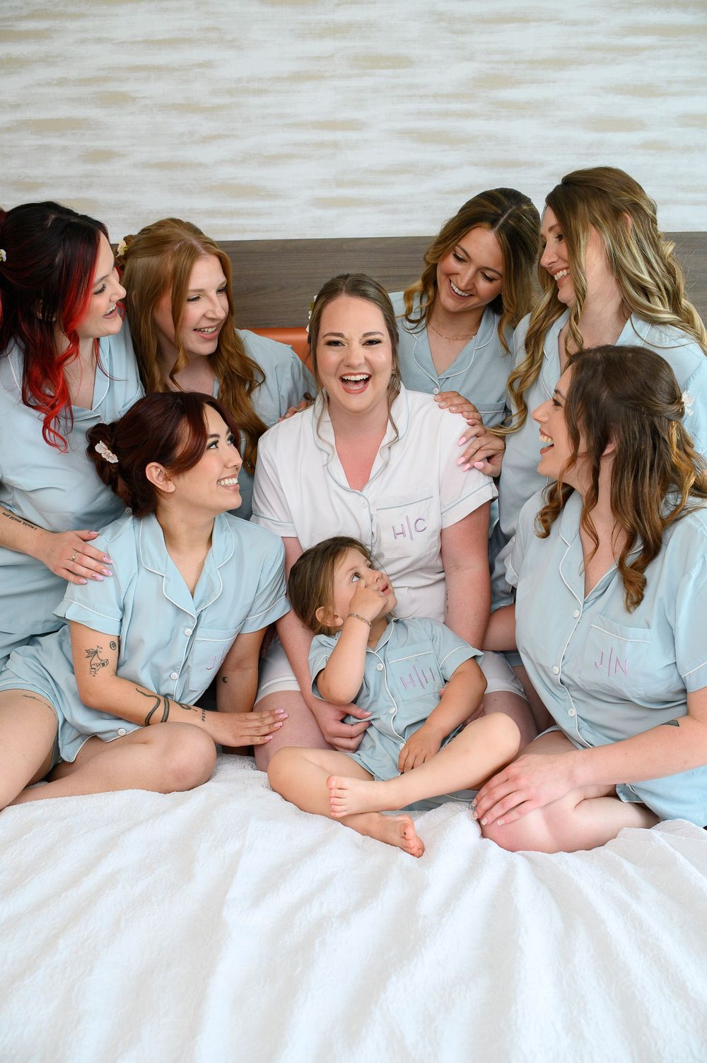 Group dressed in matching light blue button-down pajamas share laughs together while sitting on a white bed.