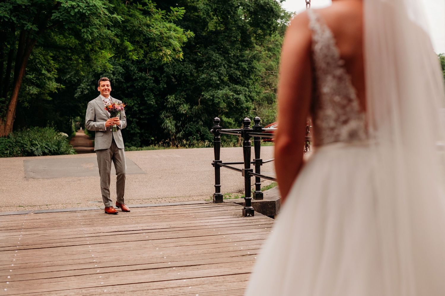 A couple in wedding attire shares an intimate slow dance on an outdoor wooden deck surrounded by trees.