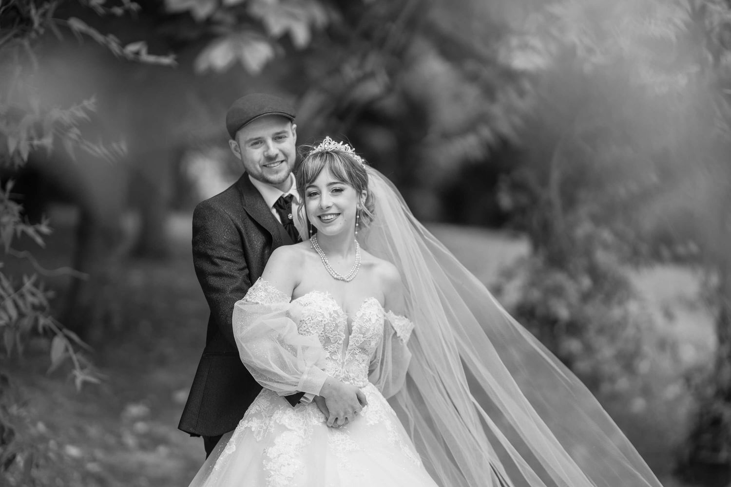 A joyful black and white wedding photo captures a happy couple outdoors with the bride holding a bouquet.