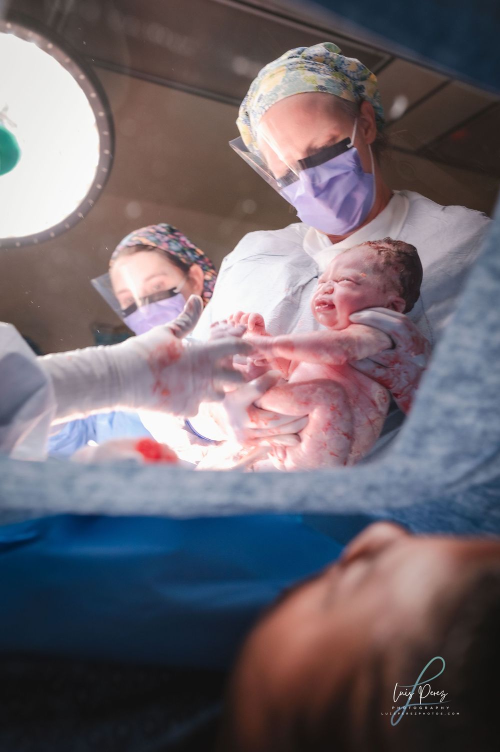 Medical team rushes to tend to a newborn baby in a hospital surgical ward under bright operating lights.