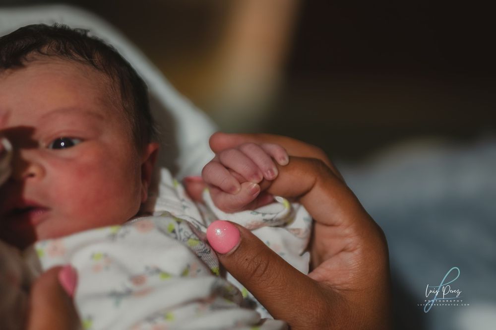 A small baby yawns while being lovingly held by supportive hands.