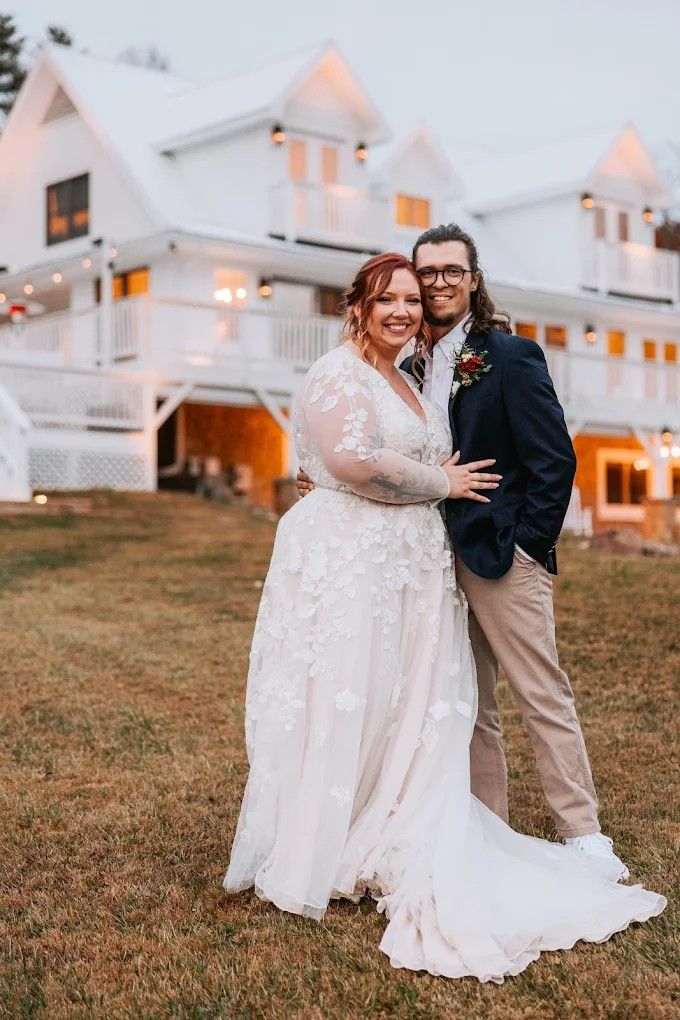 Two people share a romantic moment outdoors with white houses in the background as the sun sets.