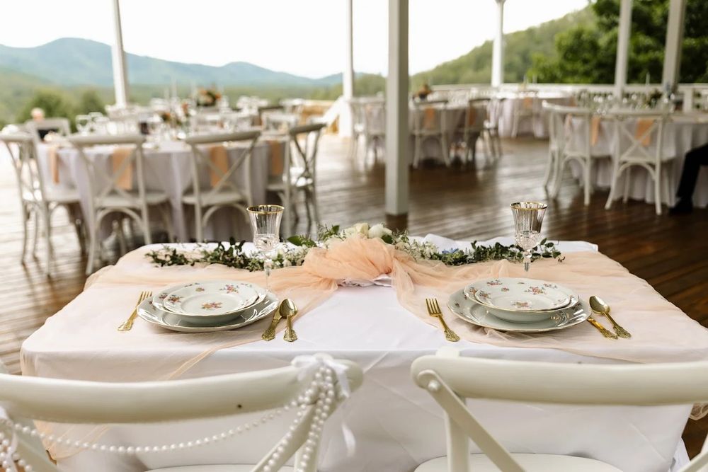 Elegant table settings with peach linens and crystal decor at an outdoor wedding reception venue with mountain views.
