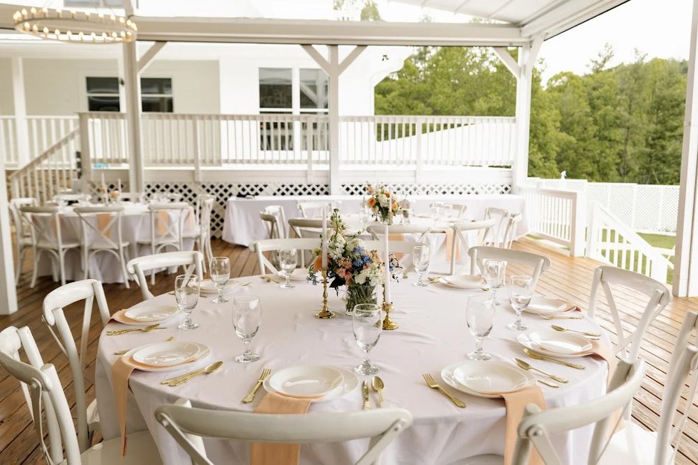 Elegant wedding reception setup on white porch with round tables and floral centerpieces under covered outdoor pavilion.