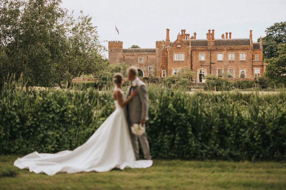 A romantic outdoor wedding at a historic brick manor house with a flowing bridal gown train spanning across expansive lawns.