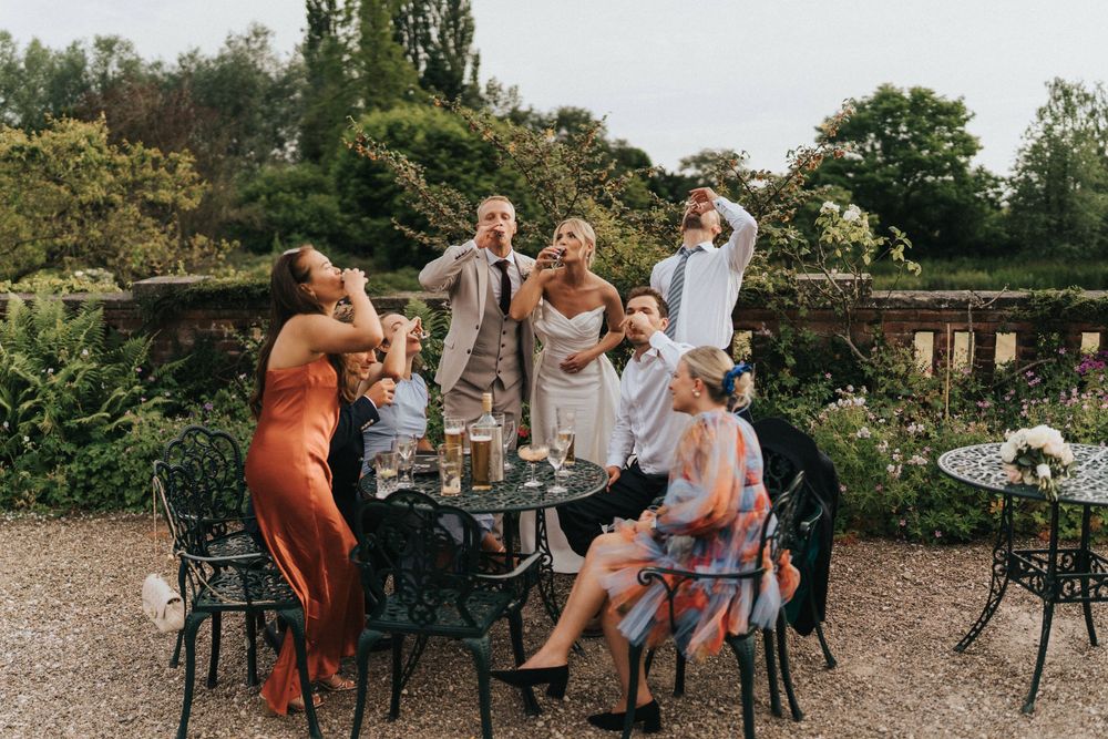 Group enjoying drinks and conversation at an outdoor garden patio table surrounded by lush greenery.