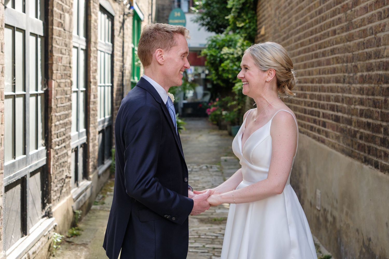 A bride and groom share a romantic moment on a cobblestone street between brick buildings.