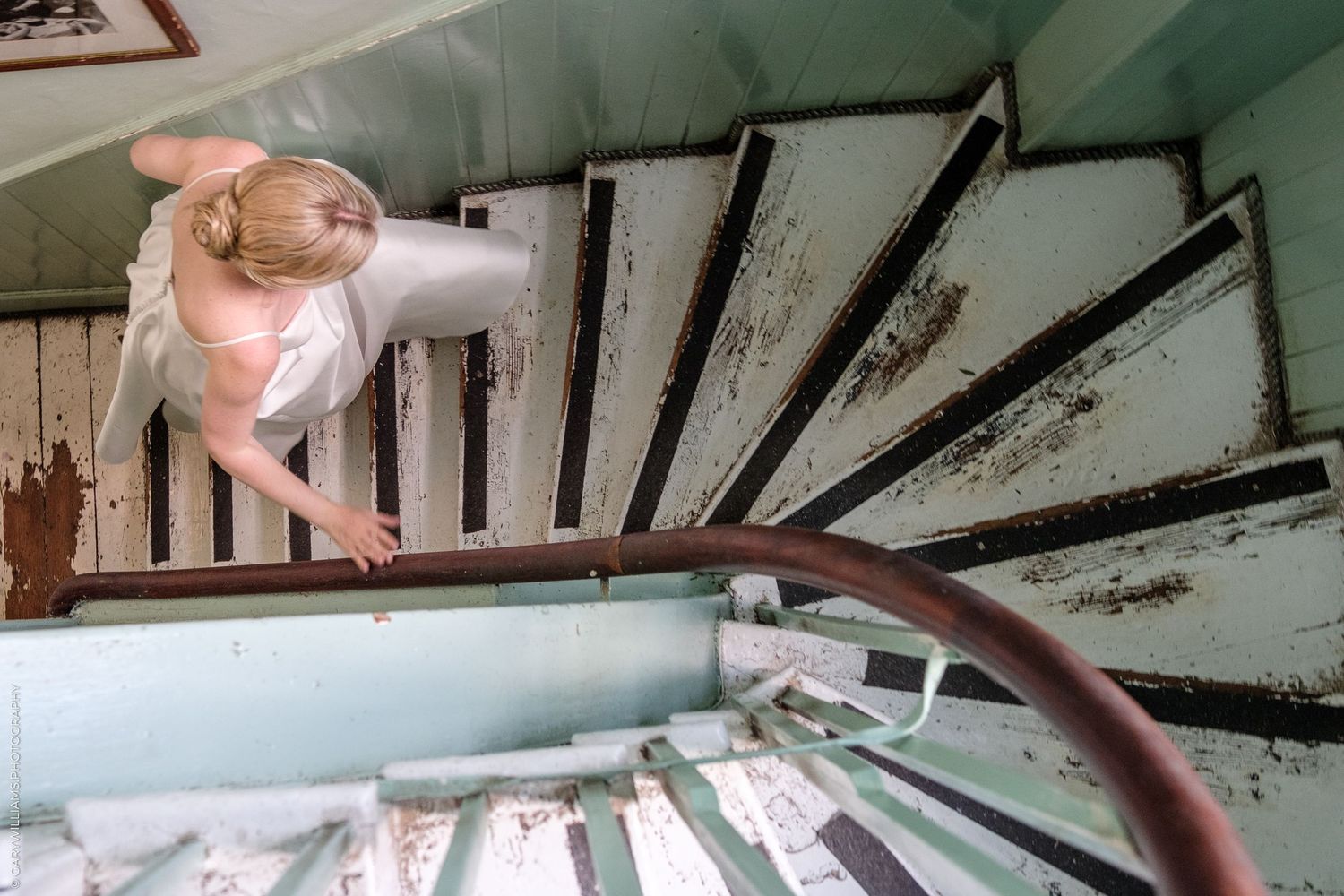 View looking down a vintage staircase with weathered white paint and dark wooden handrail showing architectural details.