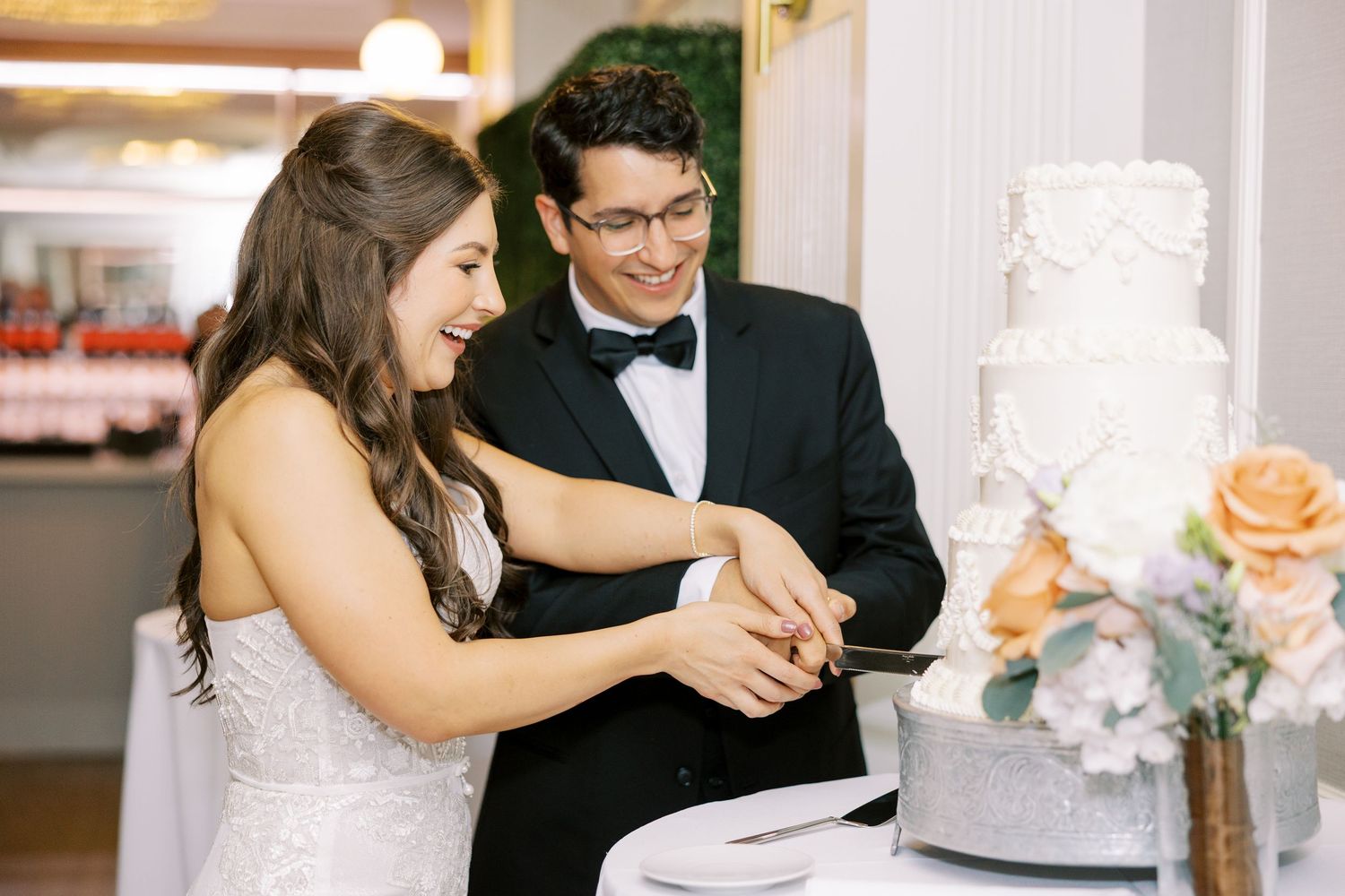 A couple in formal wedding attire cut their elegant white tiered cake together during their reception celebration.