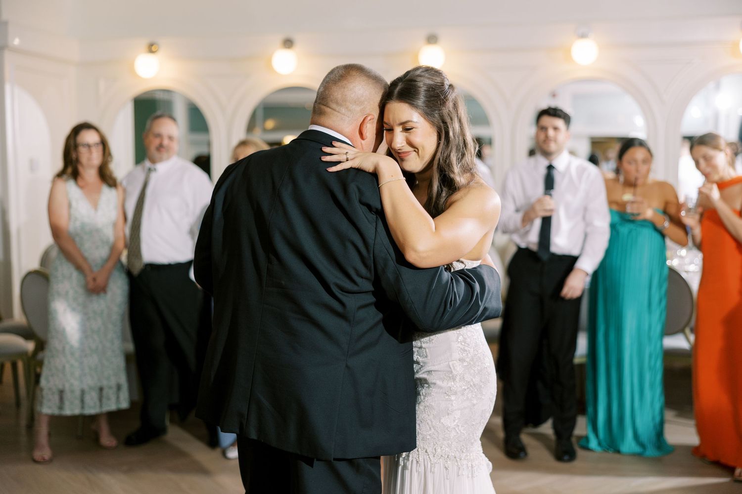 A couple shares an intimate first dance at their wedding reception while guests watch from the background in an elegant venue.