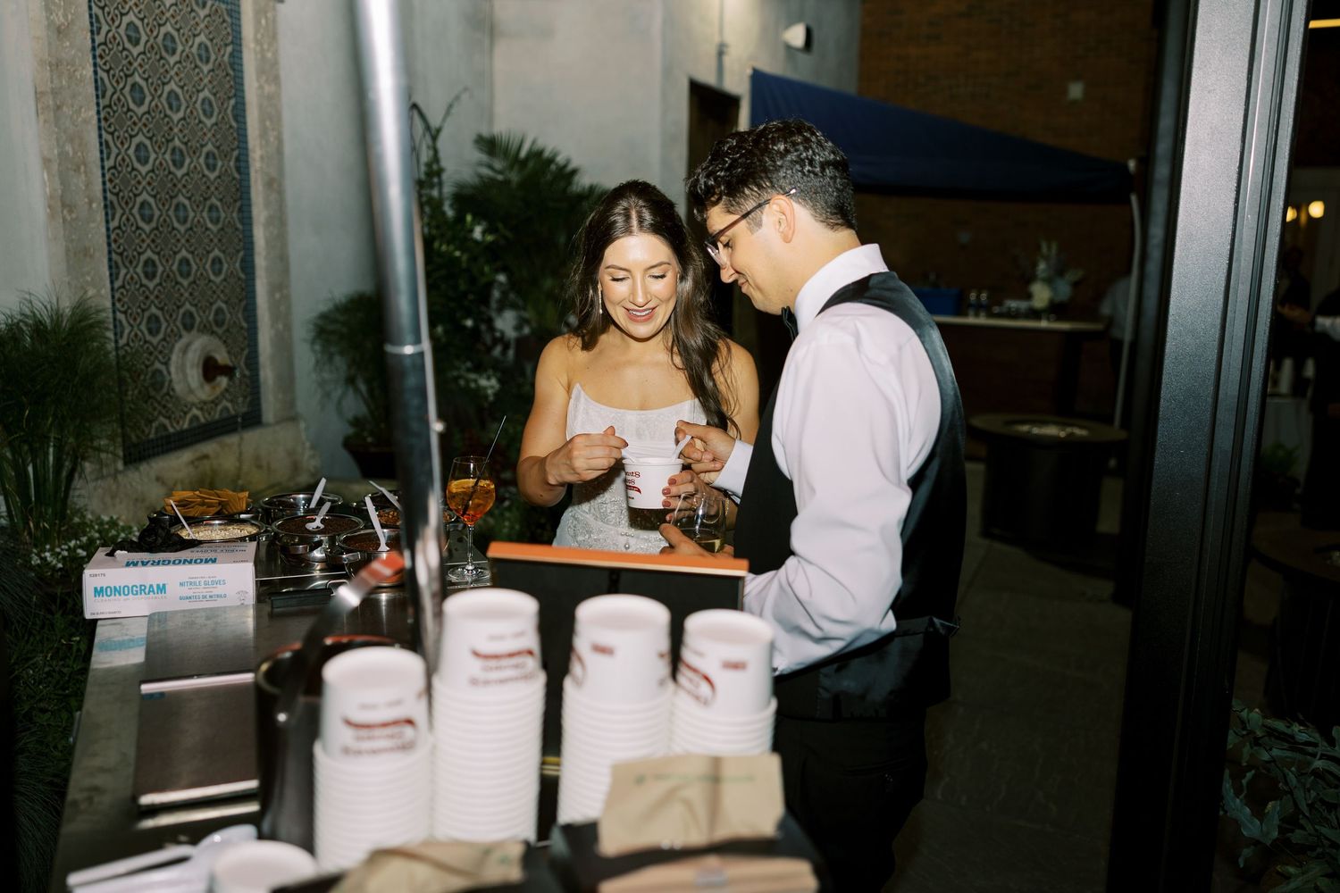 A couple serves dessert at a wedding reception buffet table filled with white cake boxes and treats.