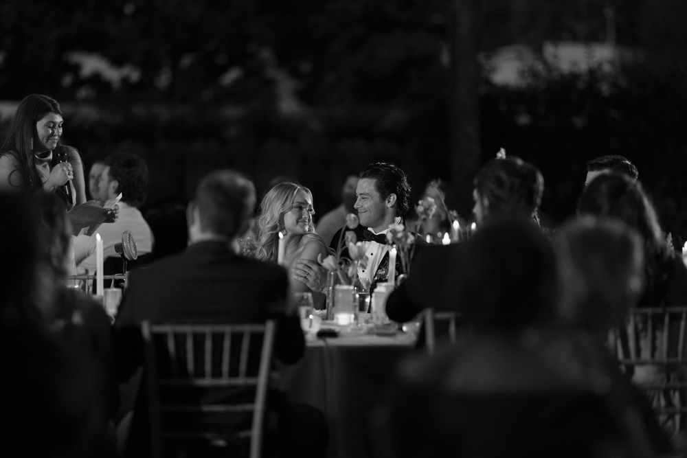 Black and white panoramic shot of a wedding reception hall with guests seated at decorated tables during an event.