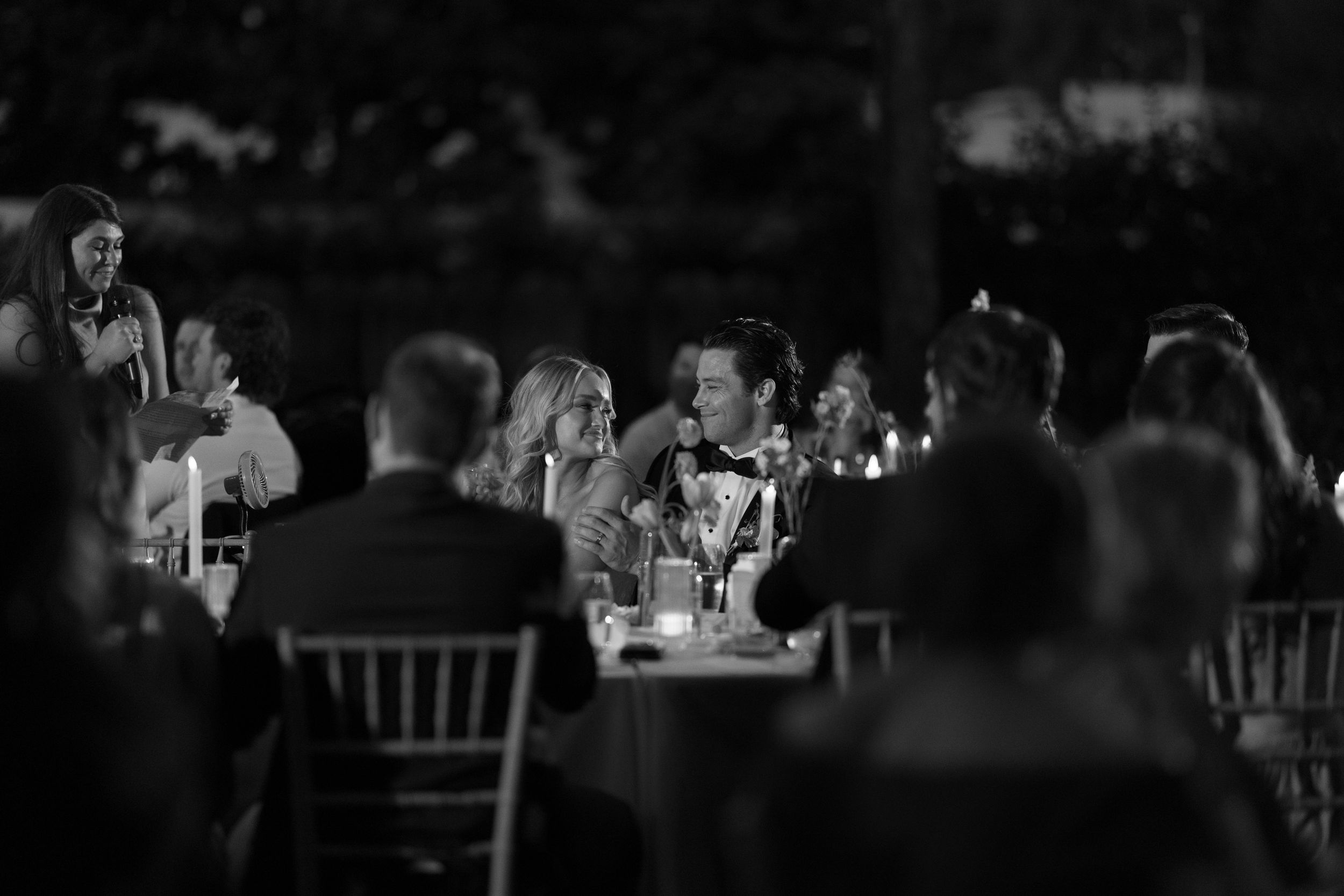 Black and white panoramic shot of a wedding reception hall with guests seated at decorated tables during an event.