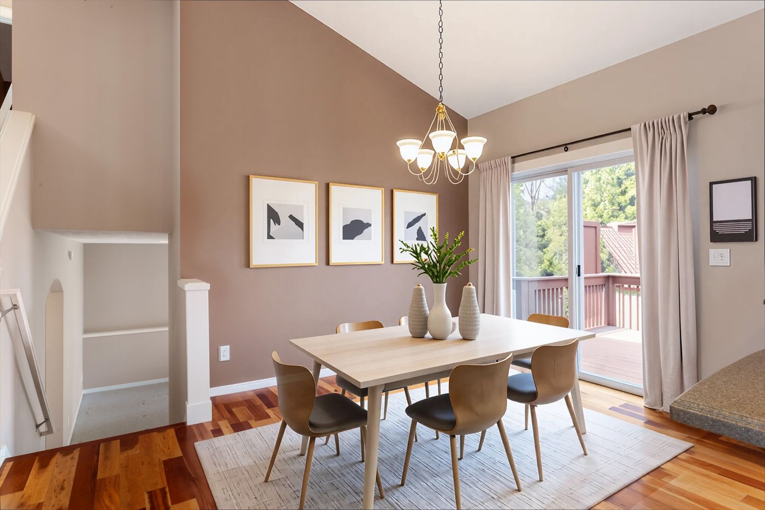 Virtually staged dining room with modern table, wood chairs, pendant lighting, warm neutral walls, and sliding door to outdoor deck.