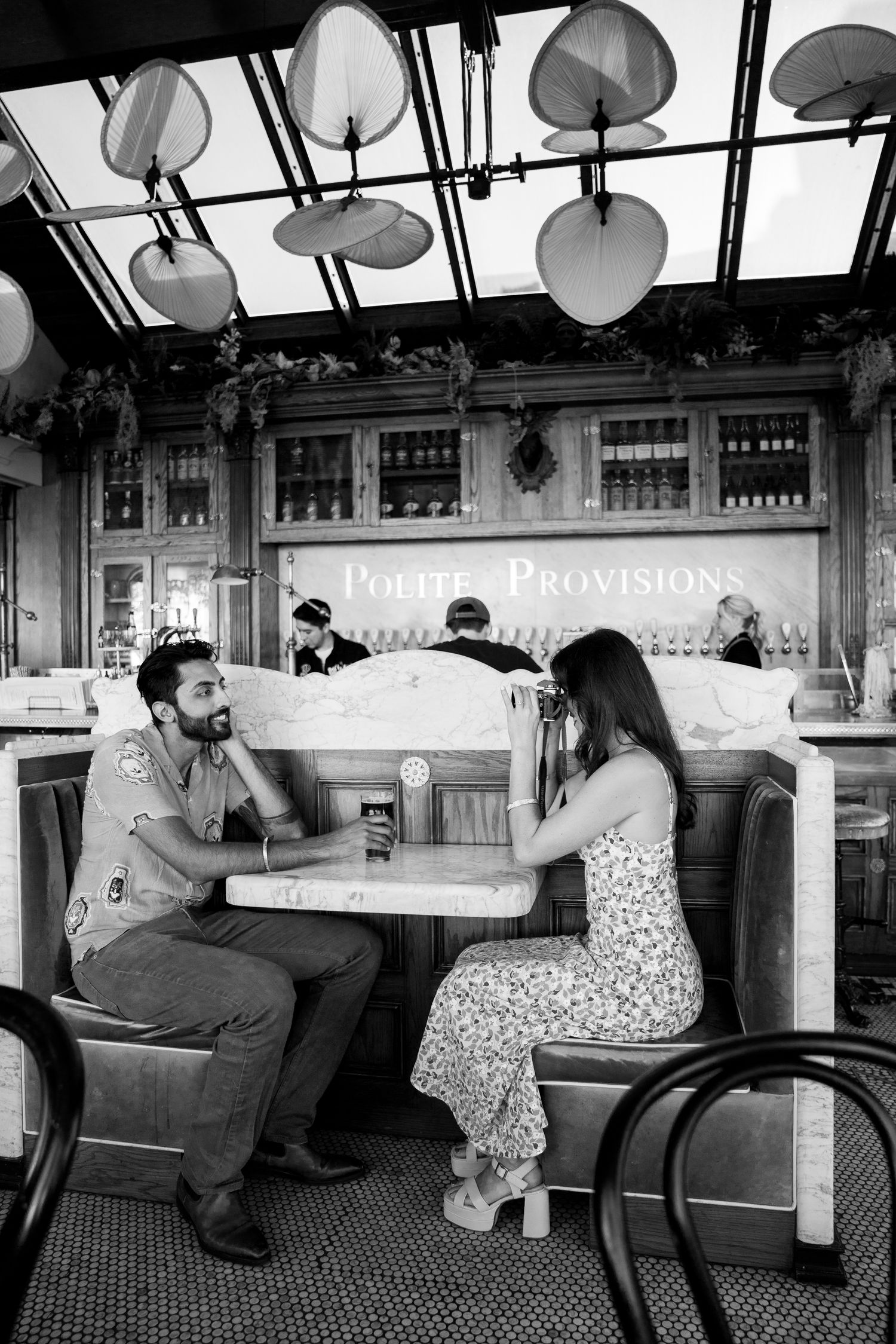 A couple sits at a restaurant booth having drinks under distinctive pendant lighting and decor in black and white.