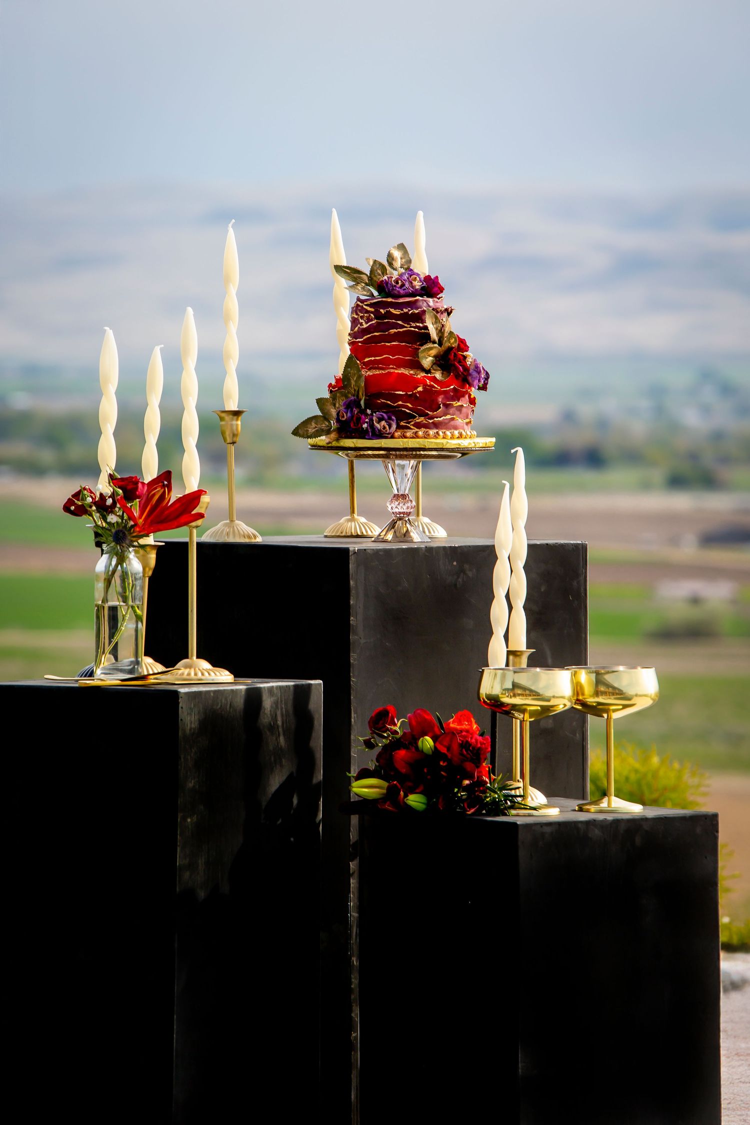 black pillars with red, orange and purple florals, white candles, gold accents, and a red and purple wedding cake