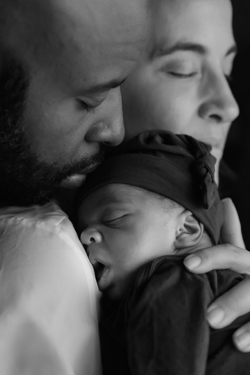 A tender black and white portrait captures an intimate family moment with a sleeping newborn baby.