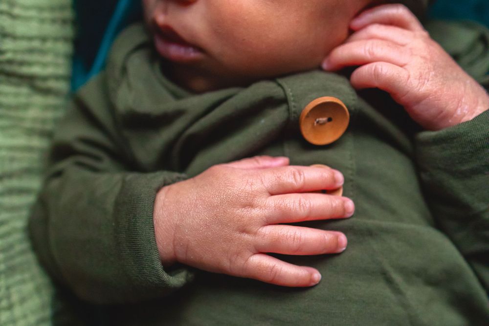 Close-up detail of small hands holding a brown button on olive green fabric clothing.