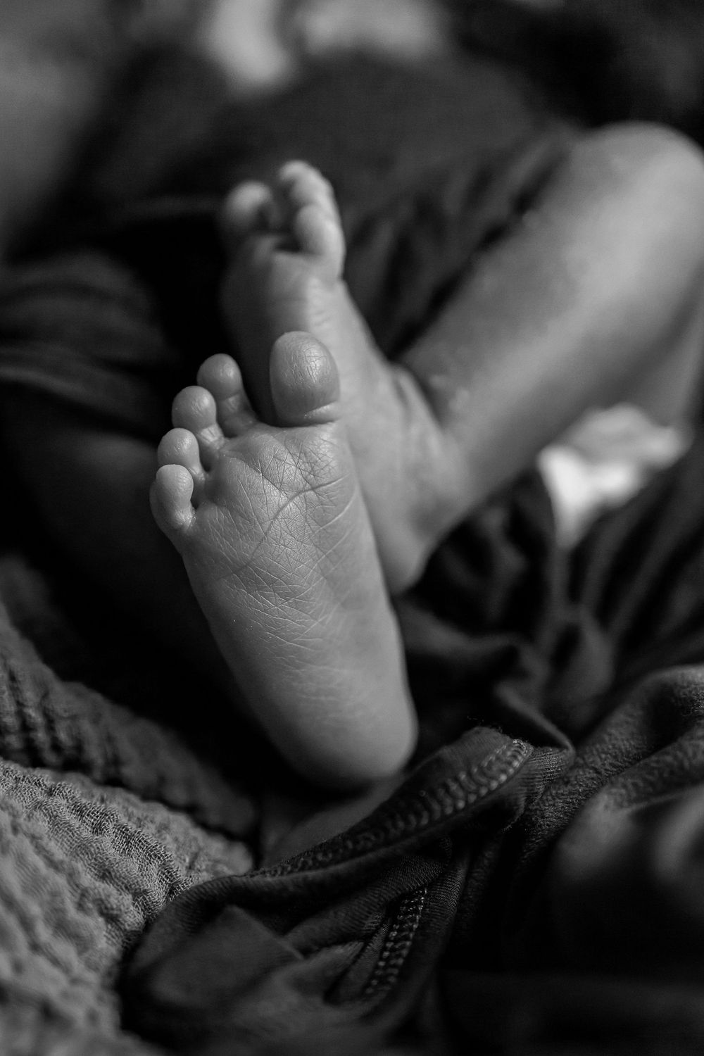 Black and white close-up photograph of a tiny baby foot resting on textured fabric in soft natural lighting.
