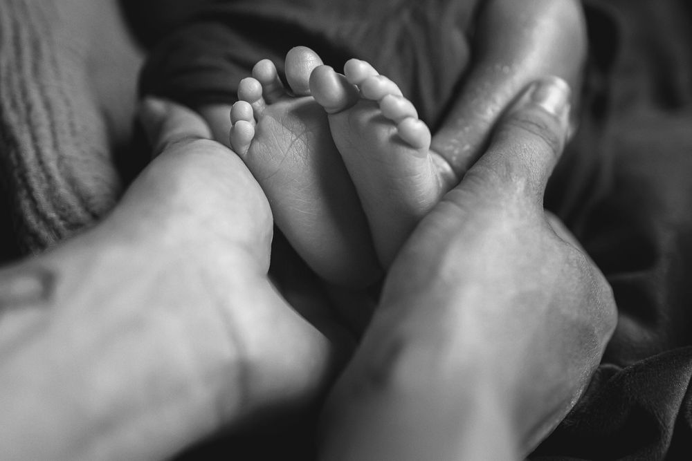 Black and white close-up photo of tiny baby feet being gently held in adult hands.