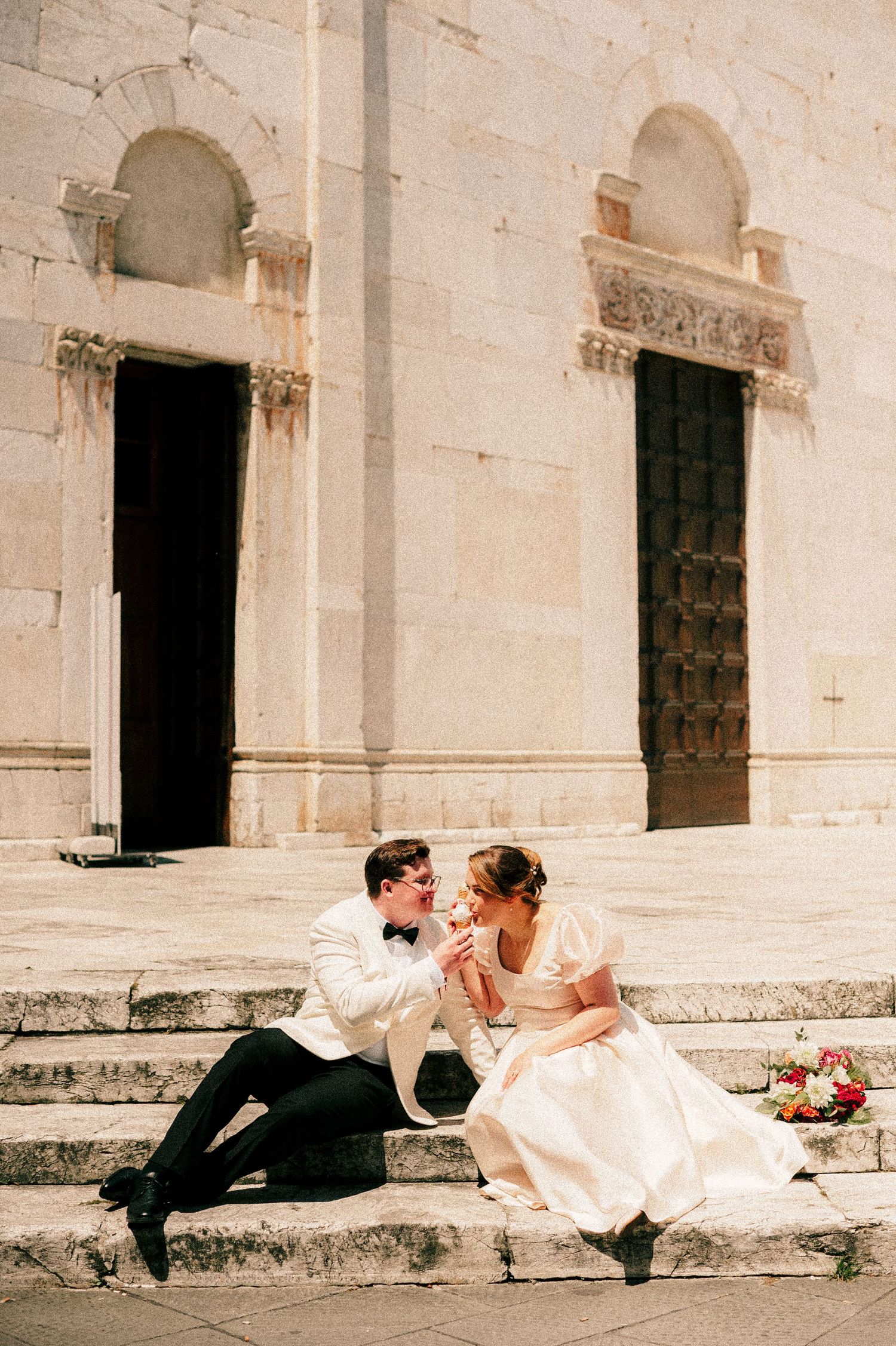 A couple sitting on stone church steps sharing an intimate moment in formal attire.