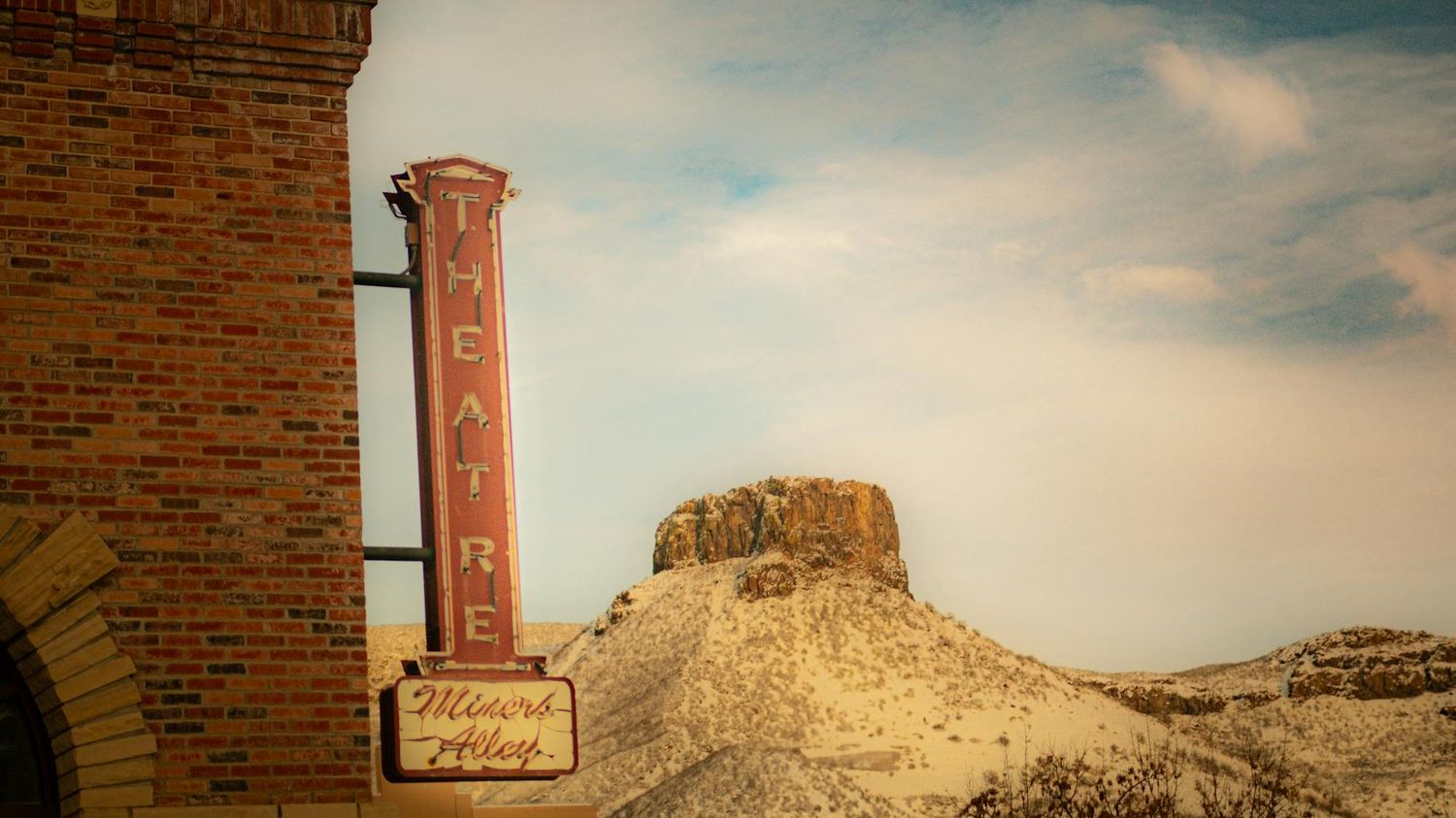 A rustic western scene with a tall brick column and rugged desert mesa formation in the background.