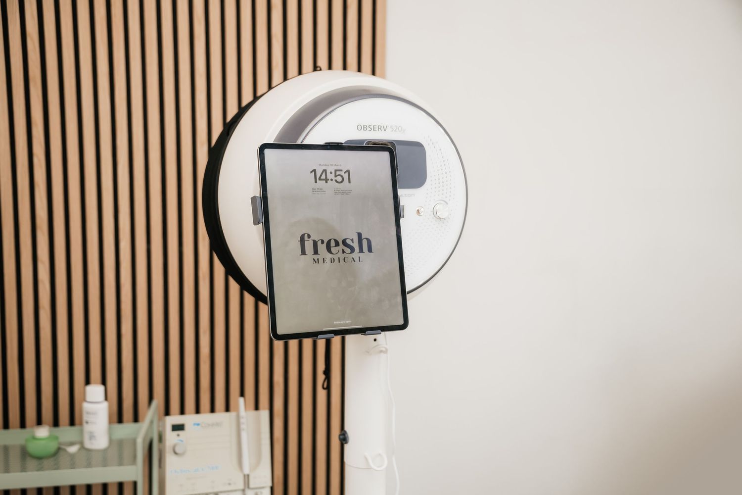 A modern electronic hand dryer mounted on a wall with vertical wooden slats features a Fresh brand display screen.
