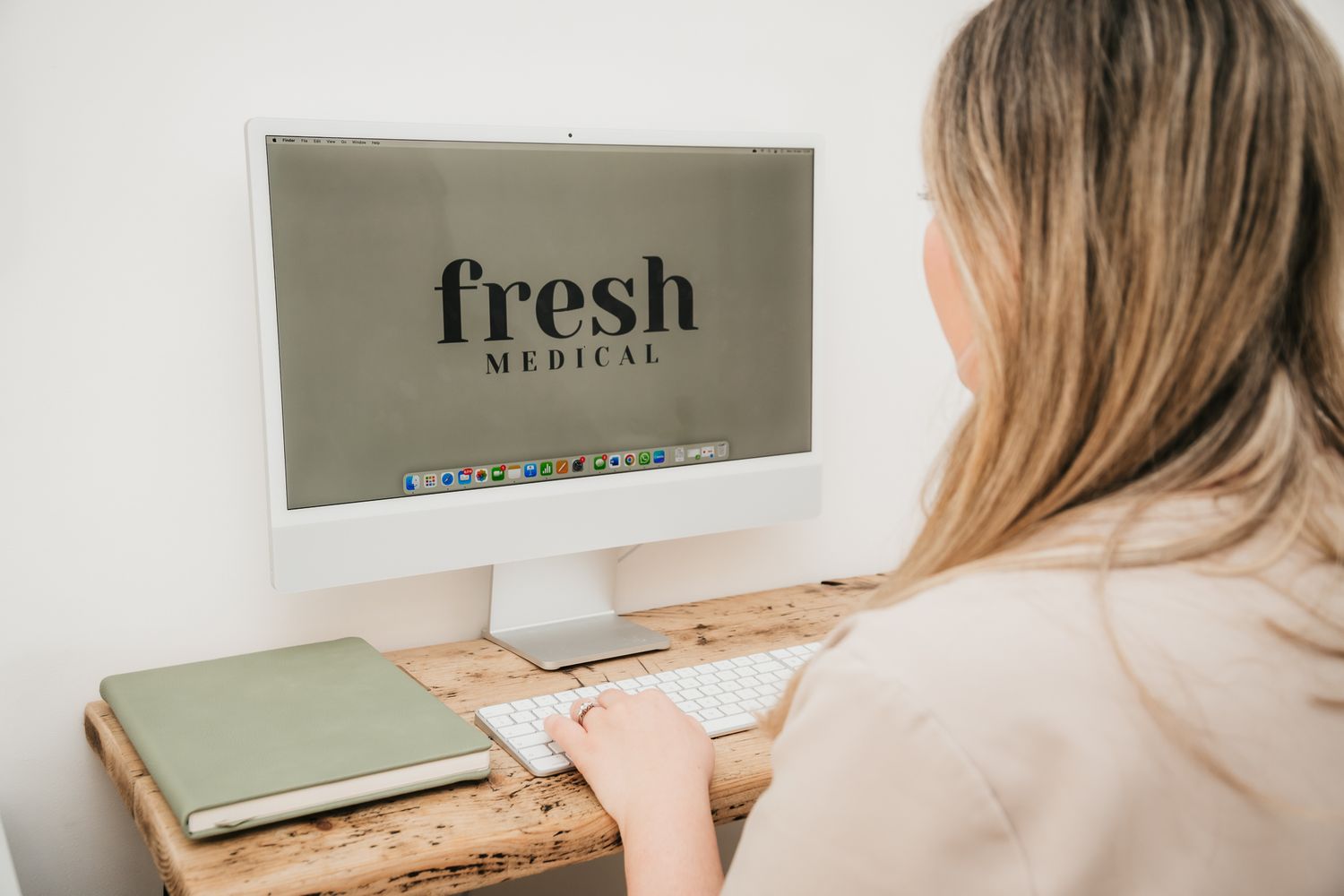 Someone in a beige sweater working at a wooden desk with a computer monitor displaying text that says 'fresh'.