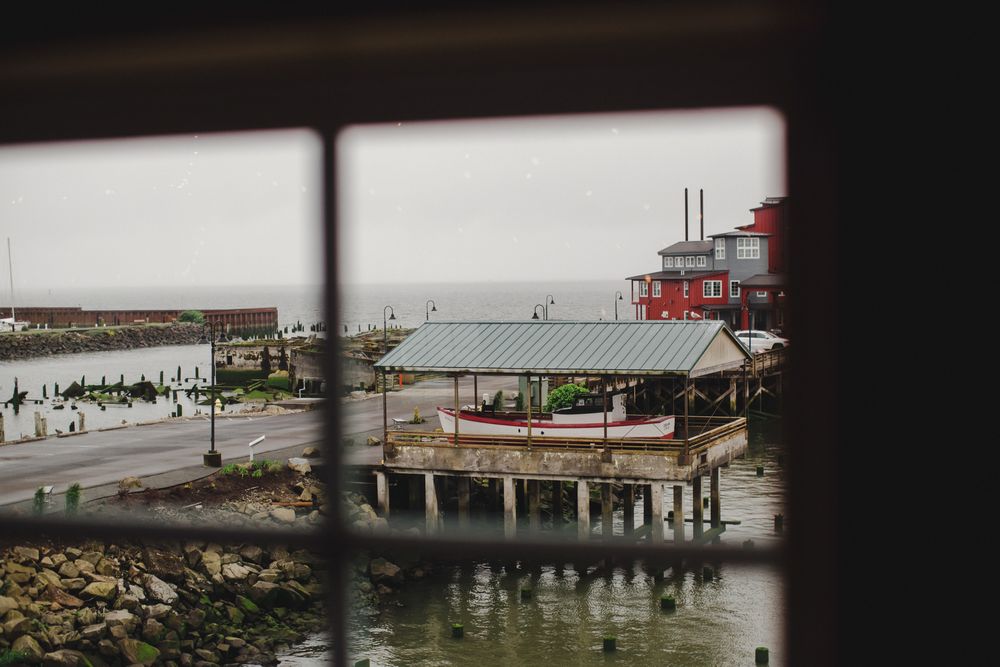 View through window of a coastal restaurant pier with red roof overlooking a waterfront boardwalk and harbor.