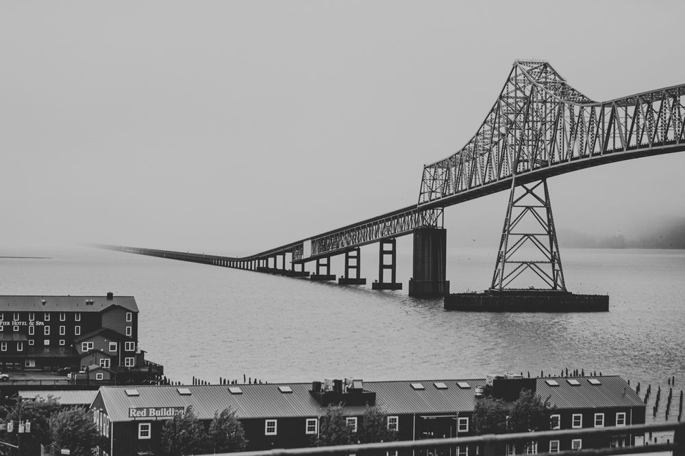 Black and white cityscape view of the Astoria-Megler Bridge spanning across the Columbia River.