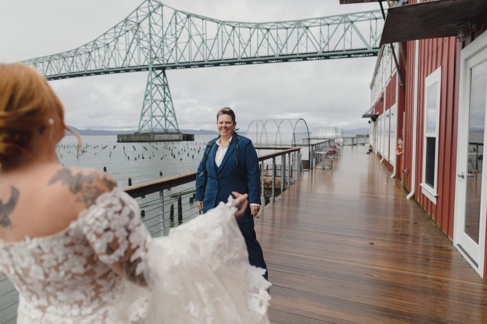 Two people share a romantic moment on a wooden deck with the Astoria-Megler Bridge in Oregon visible in the background.