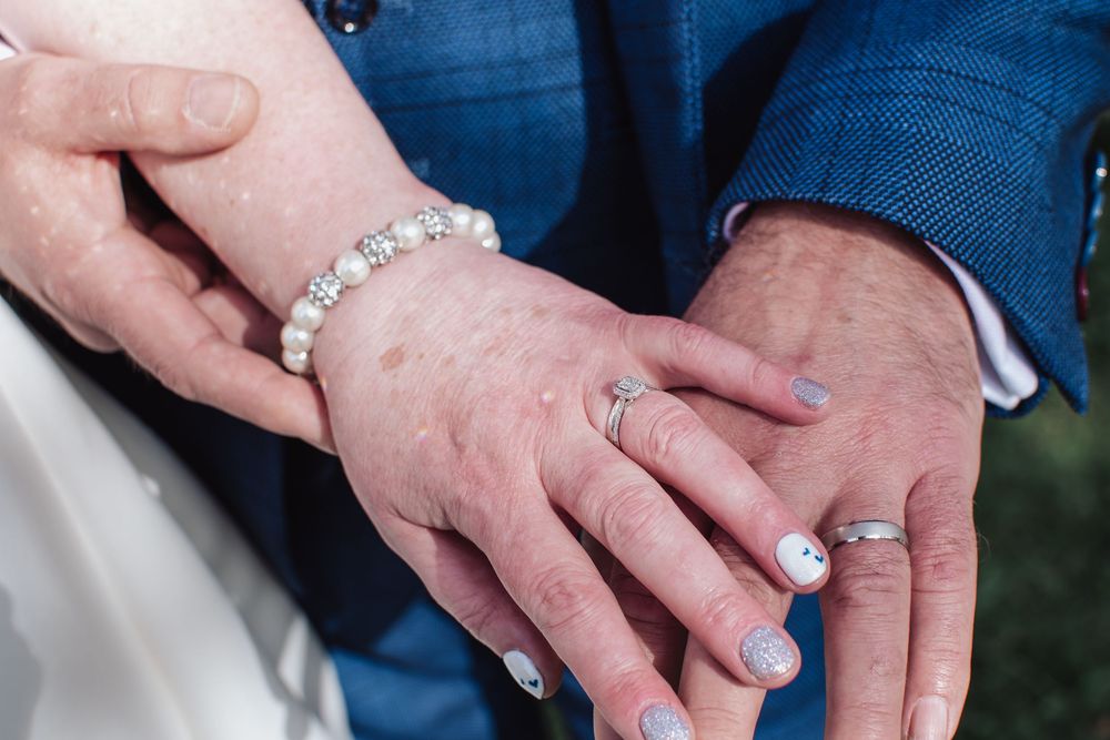 Close-up of hands showing off wedding rings and bracelet against blue formal attire.
