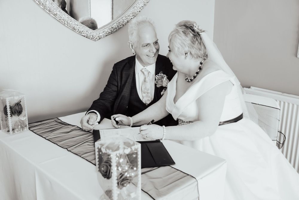 A black and white photograph of two older people sitting at a table and signing documents together.