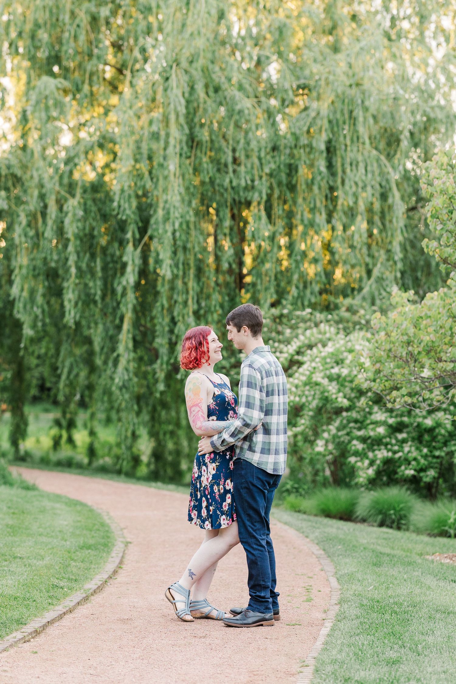 A couple embraces on a garden path beneath a drooping willow tree on a sunny summer afternoon at Cantigny Park