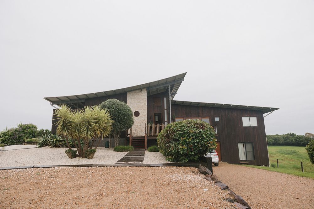 Modern angular architecture of a gray house with palm trees and gravel driveway.