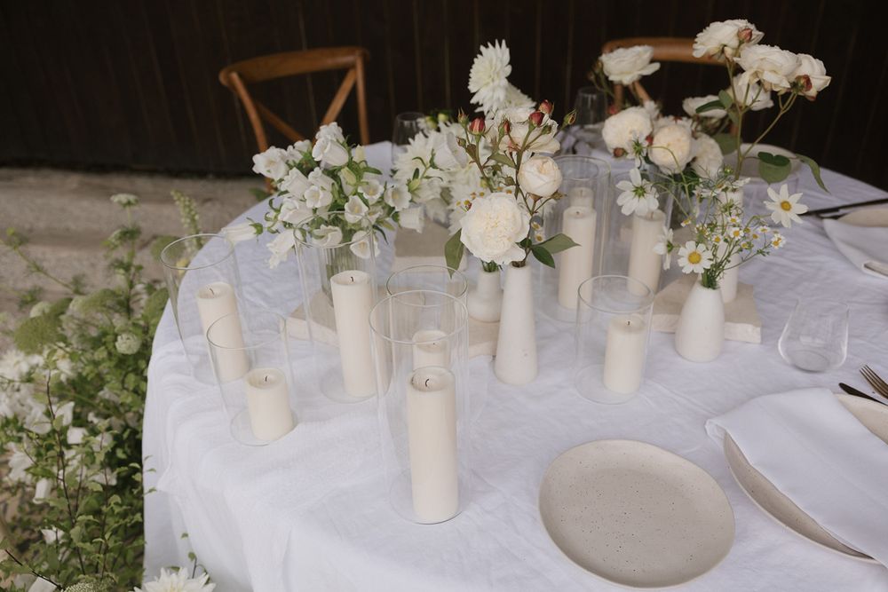 White table setting with delicate floral arrangements and cylindrical candle holders.