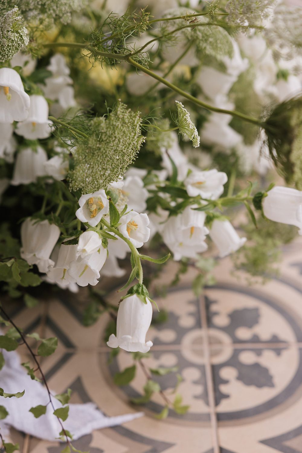 White bell-shaped flowers and greenery arranged over decorative tiled flooring.