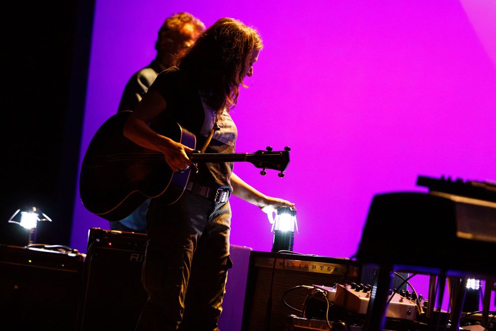 Musician performing with acoustic guitar against vibrant purple stage lighting.